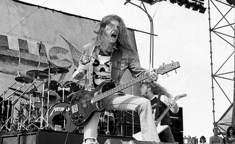 Foto de Cliff Burton mostrando su influencia punk y metal clásico con parches y camisetas de bandas icónicas.